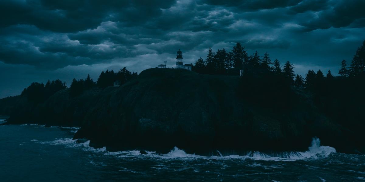 Storm clouds over a forested headland with a lighthouse.